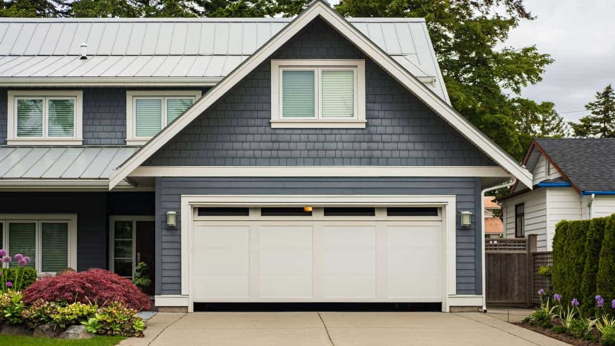Grijs huis met witte pvc garagepoort met ramen en paneeldetail.