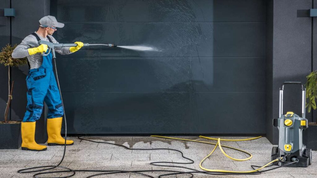 Werkman spuit garagepoort schoon

