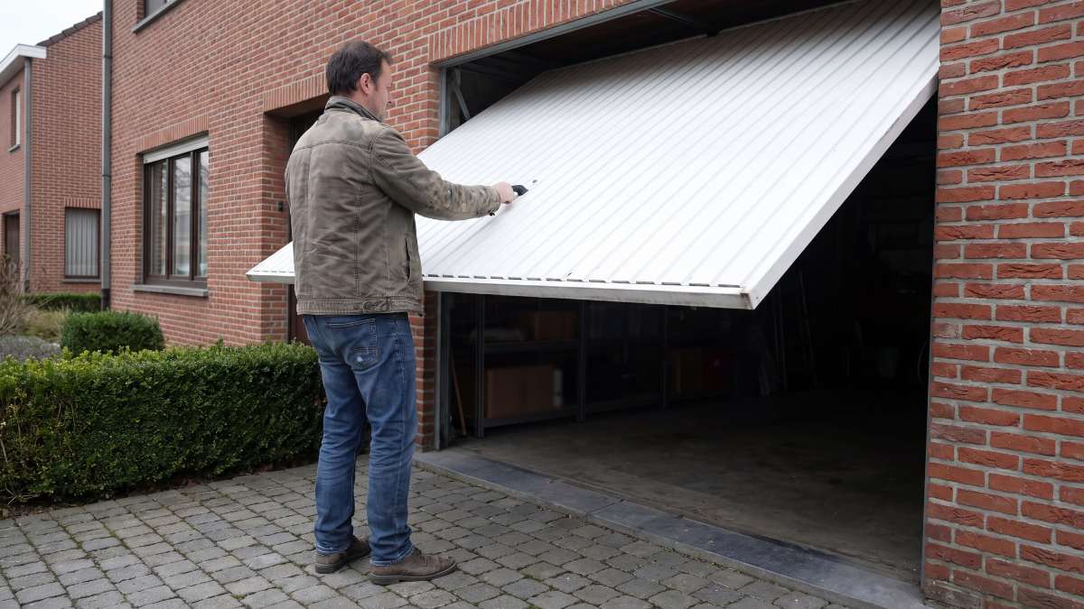 Man opent manuele witte garagepoort, bakstenen muur.