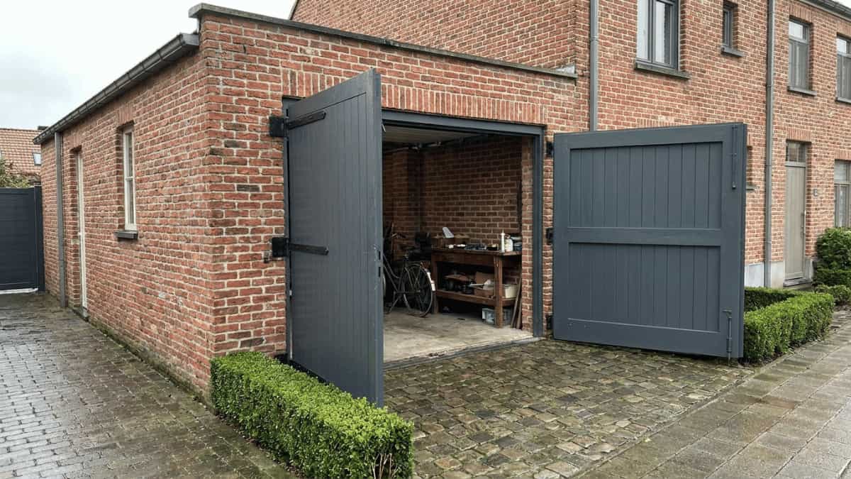 Donkere openstaande vleugelpoort voor garage bakstenen gevel